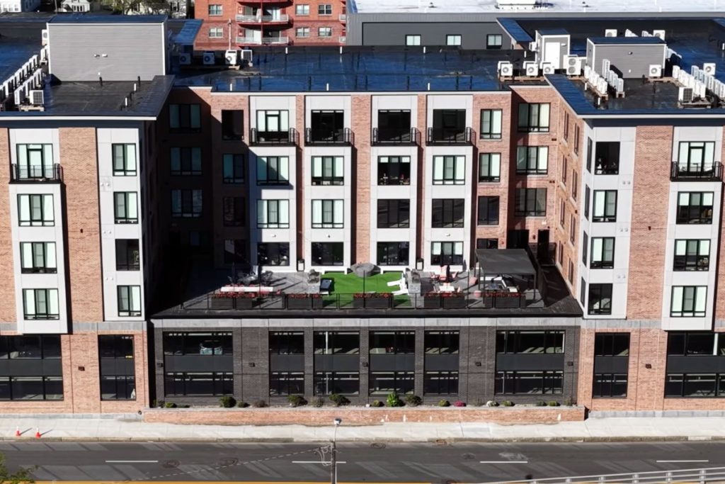 Arial view of luxury apartment complex in Quincy featuring an outdoor patio and green space above a parking garage